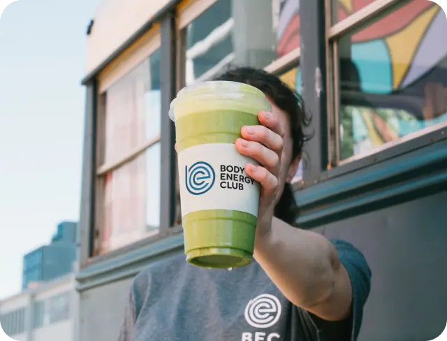 A person holding a freshly made Green Goddess smoothie from Body Energy Club